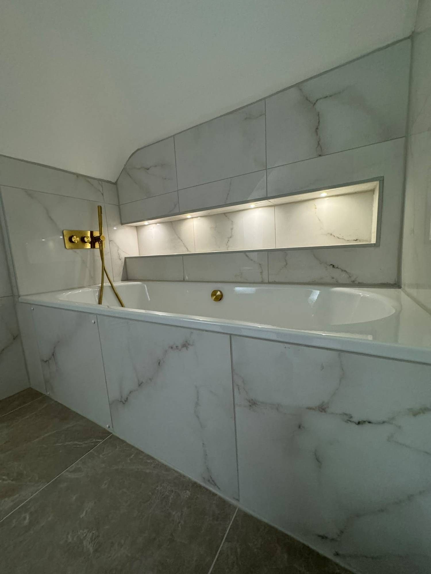 Recessed LED lighting in a marble-tiled bath niche