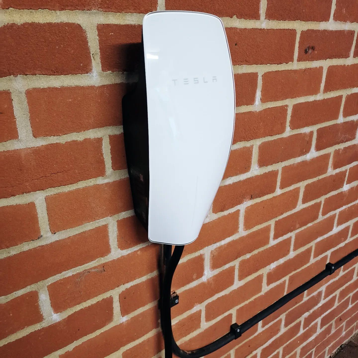 Tesla wall connector installed on a brick wall with a neat cable route