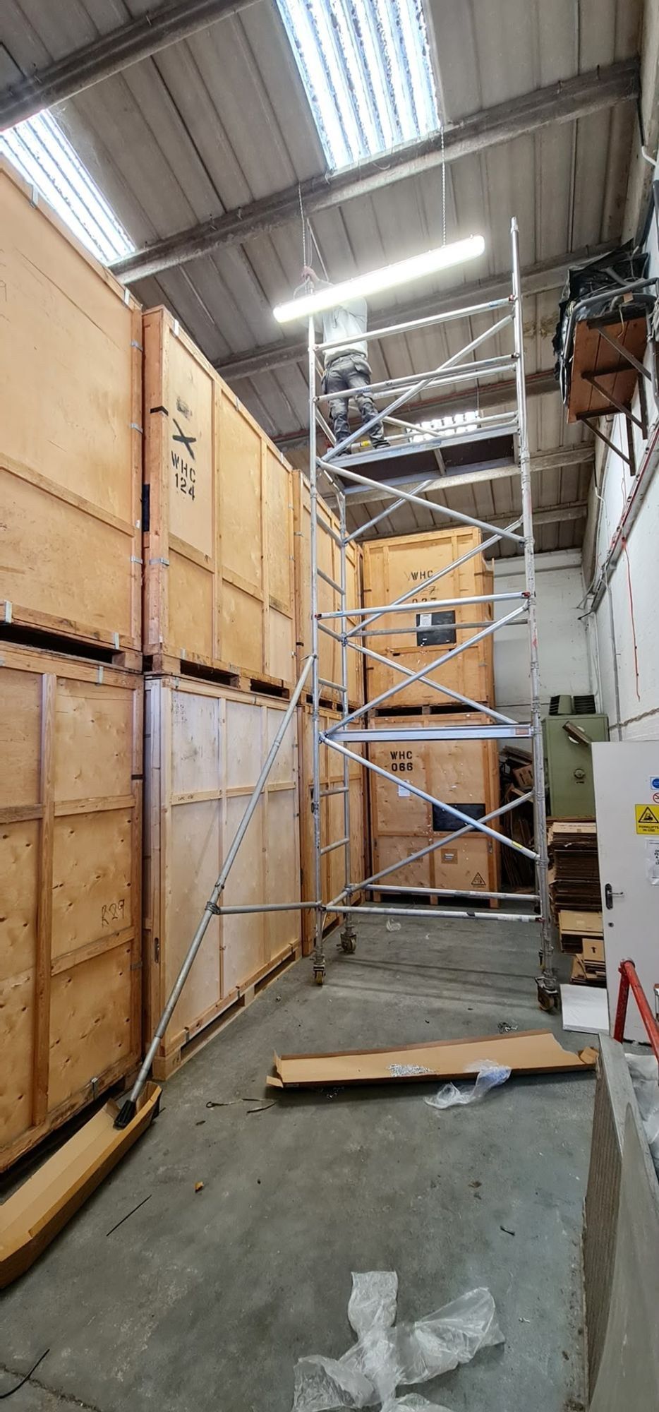 Electrician installing high-level lighting from a tower scaffold in a warehouse
